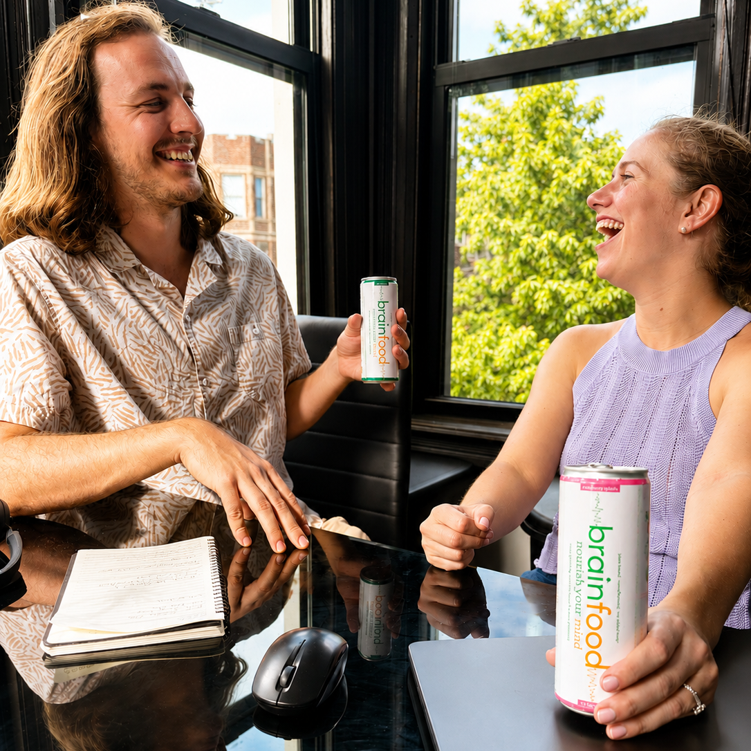 Two people sitting at a table with Brainfood energy drink and sparkling water cans