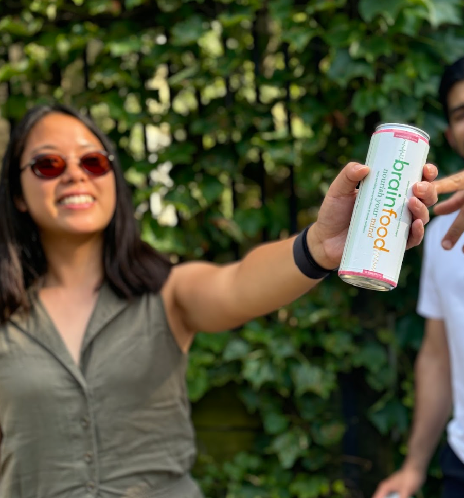 Person holding a can of Brainfood sparkling energy water in front of a green leafy background