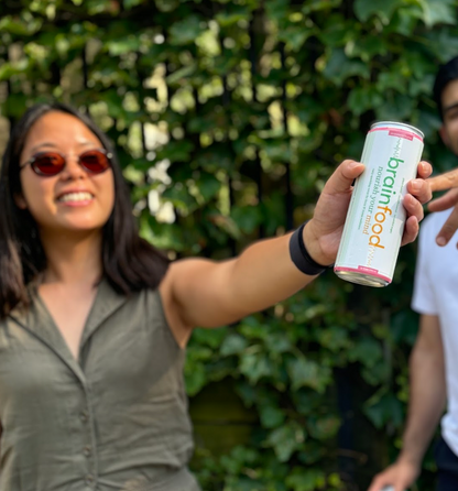 Person holding a can of Brainfood sparkling energy water in front of a green leafy background